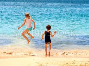 Two kids jumping in the sea waves on a sand beach - GlobePhotos - royalty free stock images