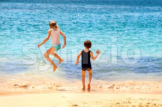 Two kids jumping in the sea waves on a sand beach Stock Photo
